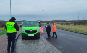 Po lewej umundurowany policjanta, w tle zielony  bus i dwie osoby stojące przy nim.