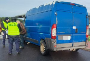 Niebieski bus, obok stoją dwaj umundurowani policjanci i kierowca.