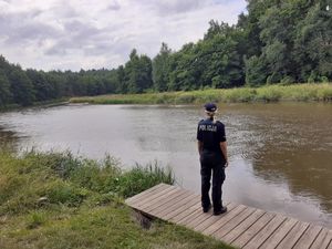 Umundurowana policjanta stojąca na pomście przy zbiorniku wodnym.