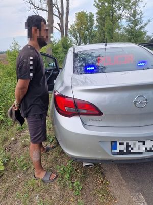 Zatrzymany mężczyzna stojący przy srebrnym samochodzie.