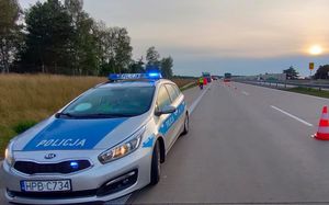 Miejsce na autostradzie gdzie doszło do śmiertelnego potrącenia kierowcy. Na pierwszym planie po lewej stornie radiowóz. W oddali samochód ciężarowy i autobus.