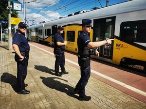 Policjant i funkcjonariusze Służby Ochrony Kolei stoją na peronie, w tle pociąg.
