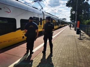 Policjant i funkcjonariusz Służby Ochrony Kolei stoją na peronie, w tle pociąg.