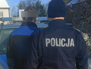 Umundurowany policjant z napisem na plecach POLICJA i stojący przed nim zatrzymany mężczyzna. Sylwetki widoczne od pasa w górę.