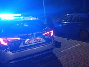 Zdjęcie zrobione w nocy, na pierwszym planie widoczny radiowóz z włączonym niebieskim światłem błyskowym, w tel pojazd osoby.
