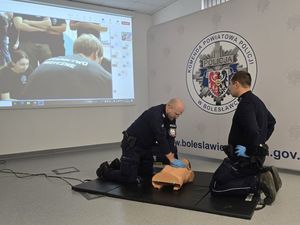 Dwóch policjantów podczas szkolenia z resuscytacji, pomiędzy nimi fantom szkoleniowy. Jedne z mundurowych uciska fantoma.