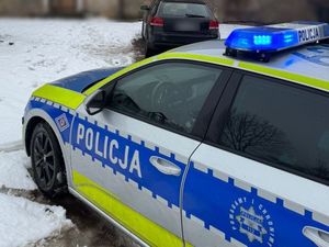 Na pierwszym planie widoczny radiowóz, na drugim czarny pojazd osobowy.