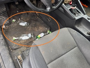 Widoczne wnętrze pojazdu od strony fotela kierowcy, a na wycieracze przed fotem leżące 3 puste szklane butelki.