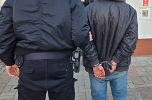 Zatrzymany z kajdankami założonymi na ręce trzymane z tyłu, prowadzony przez policjanta.