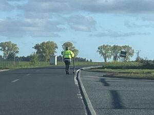 Mężczyzna w odblaskowej kurtce prowadzi hulajnogę.