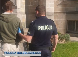 Umundurowany policjant prowadzi w kajdankach mężczyznę do budynku sądu