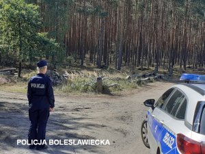 Policjantka, obok radiowóz a w tle droga do lasu