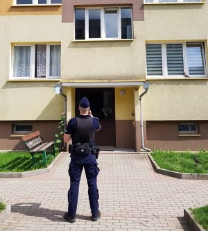 Na zdjęciu widoczny jest umundurowany policjant stojący przed blokiem